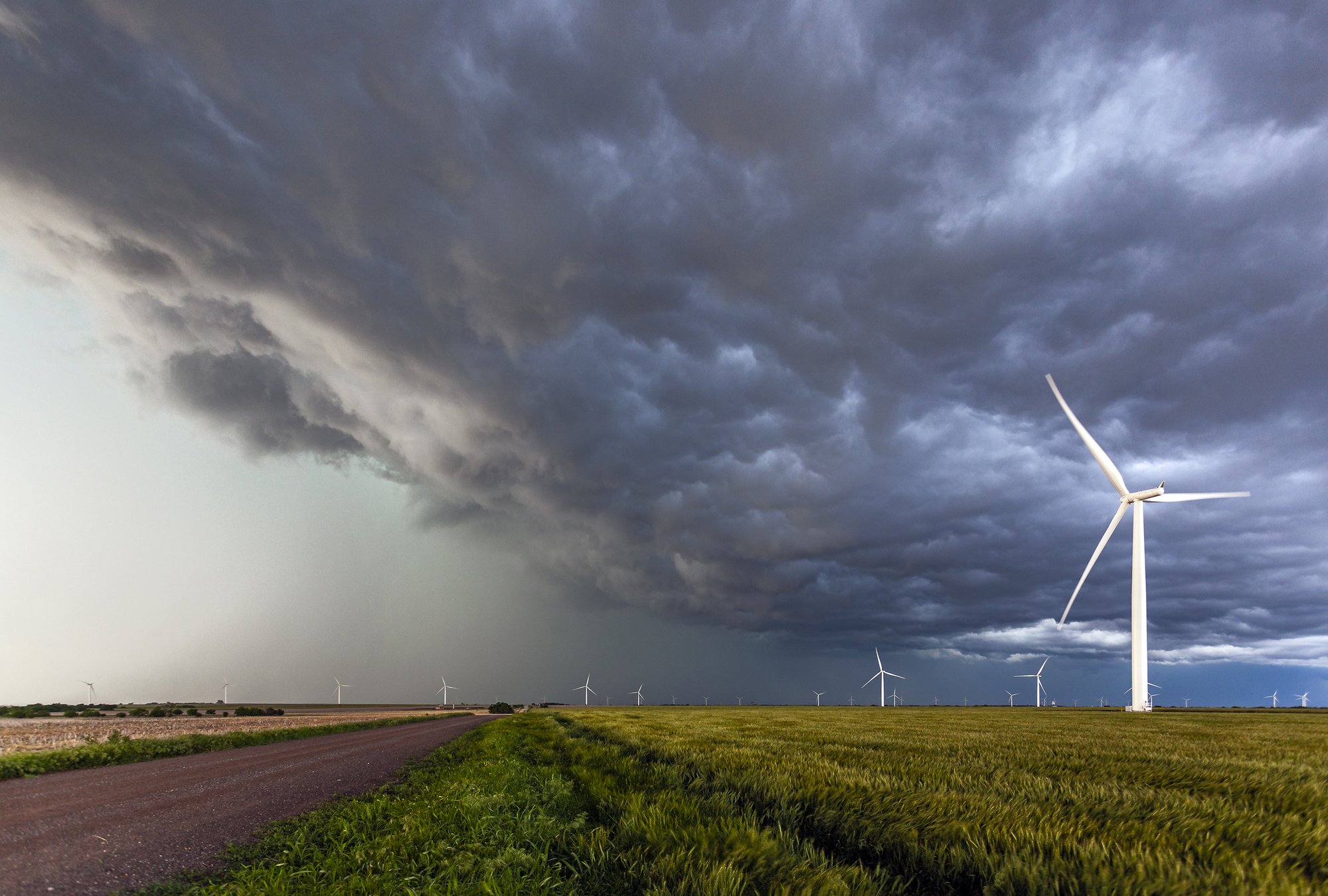 Storm system approaching wind turbines over a wheat field, representing weather and energy market risk